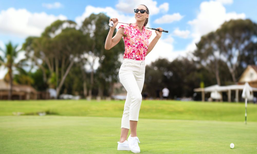 Beautiful woman wearing a red sleeveless printed golf shirt and white pants playing golf